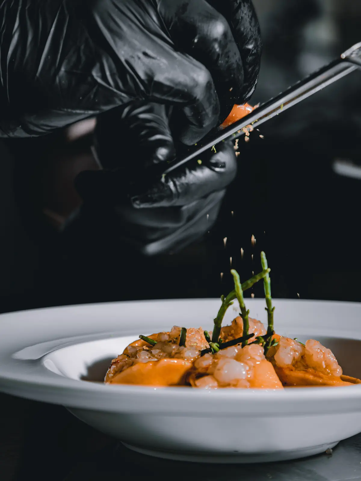 En cuisine, la touche finale : des mains gantées déposent à la pince une garniture sur une assiette de ravioles