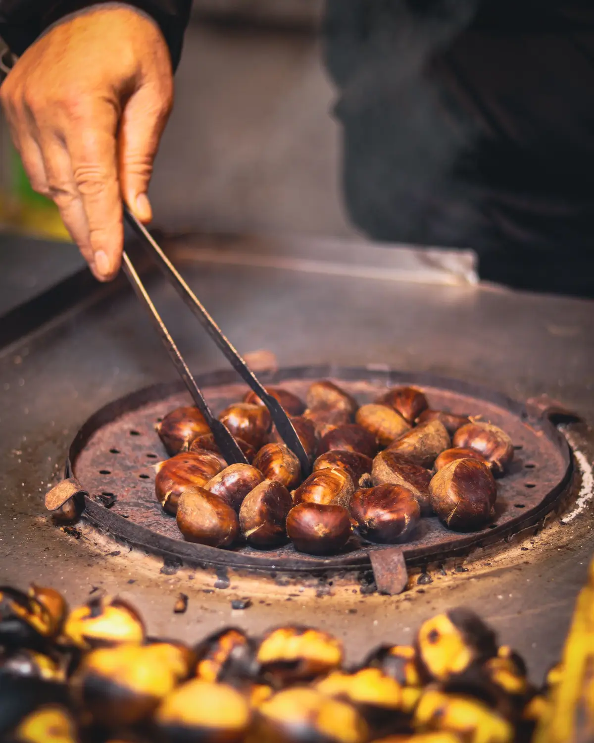 Châtaignes grillées à la pince sur une poêle percée, dans la fumée