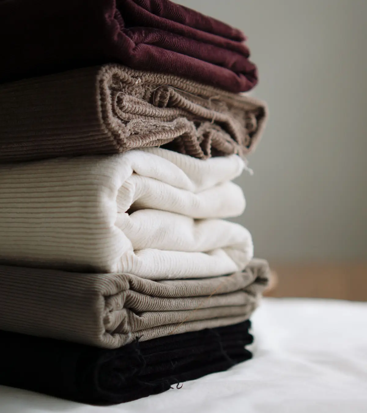Pile de tissus pliés aux tons bordeaux, taupe, écru et noir