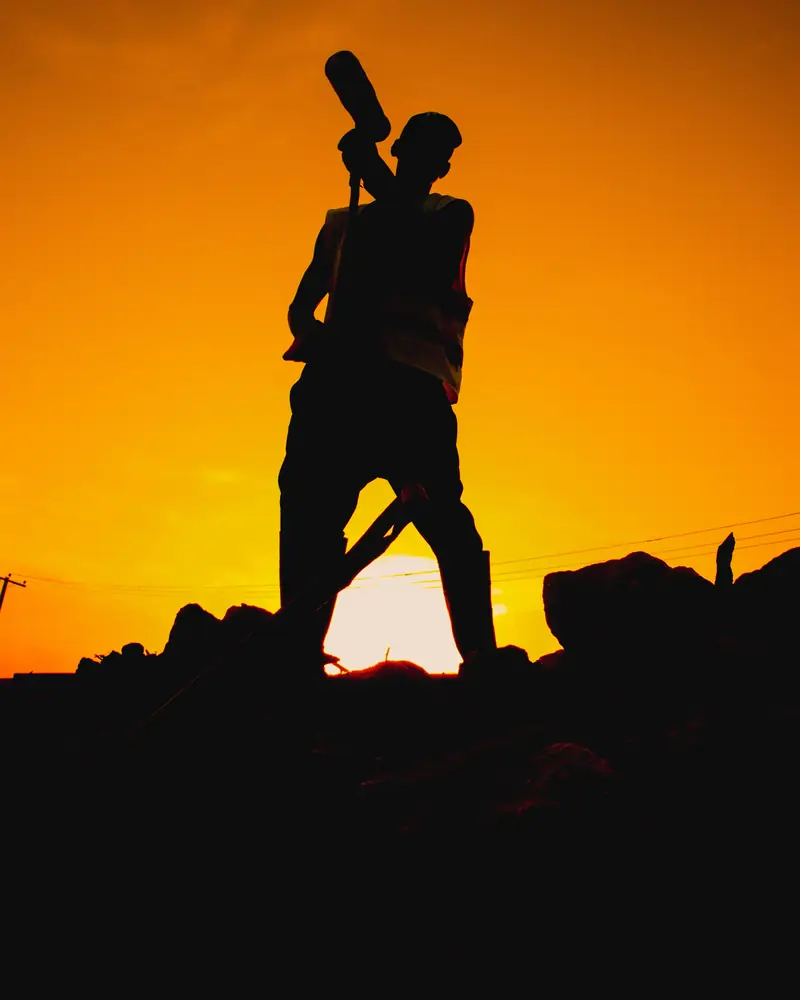 Julien : silhouette d'un ouvrier, outil à l'épaule, sur un chantier au coucher du soleil (photo d'illustration)