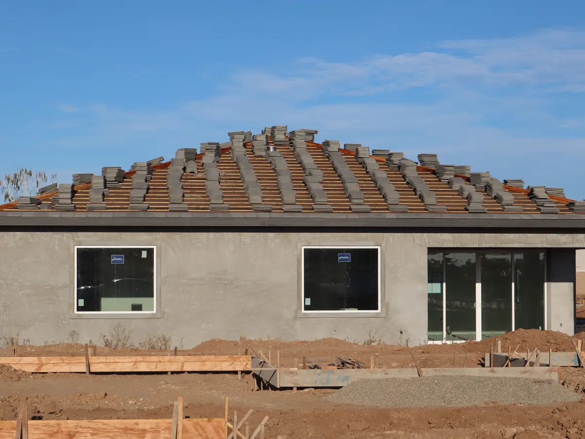 Maison de plain-pied en construction, murs enduits et tuiles en cours de pose, coffrages au pied
