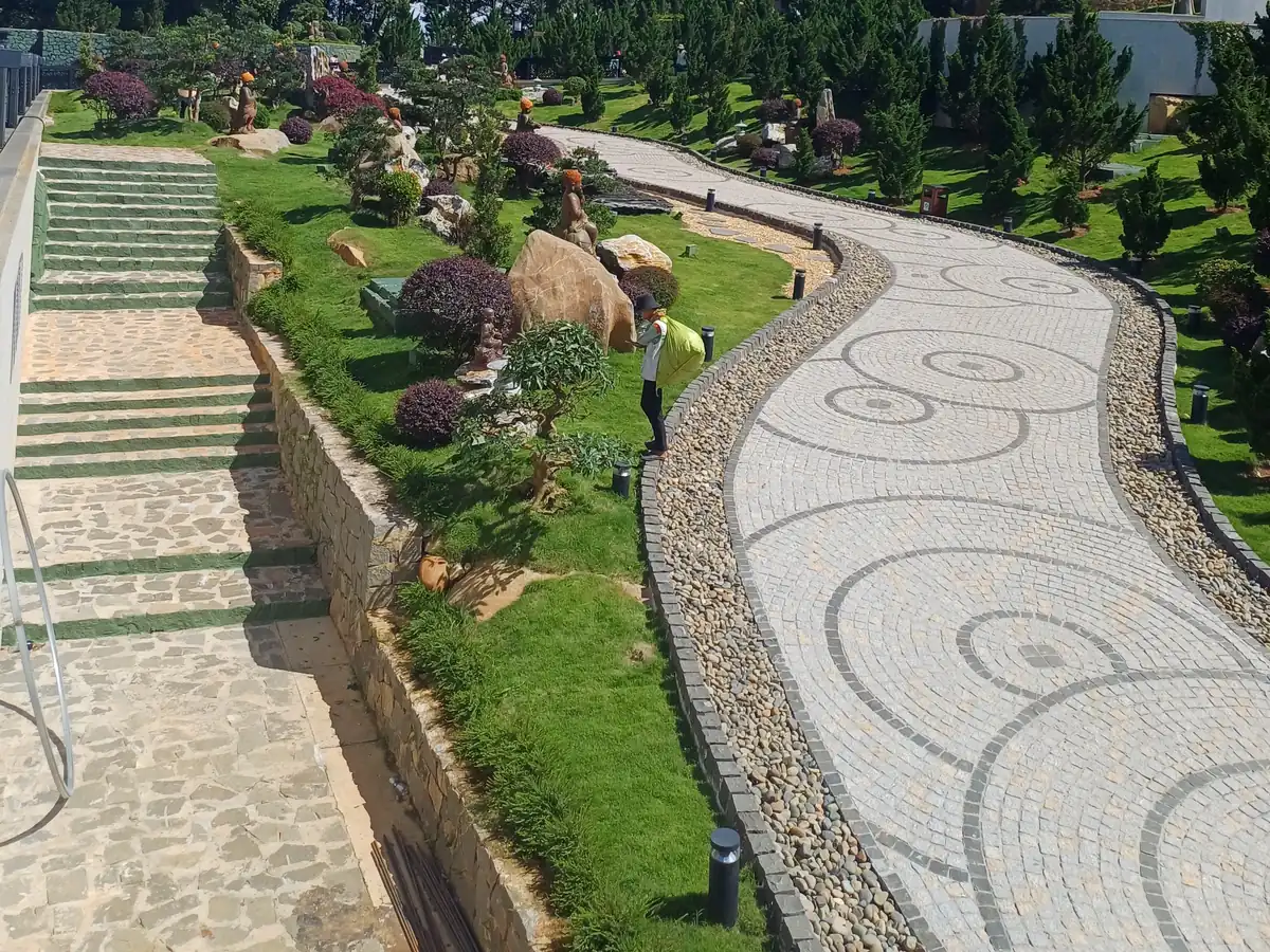 Allée pavée et escalier en pierre bordés d'un muret, dans un jardin paysager