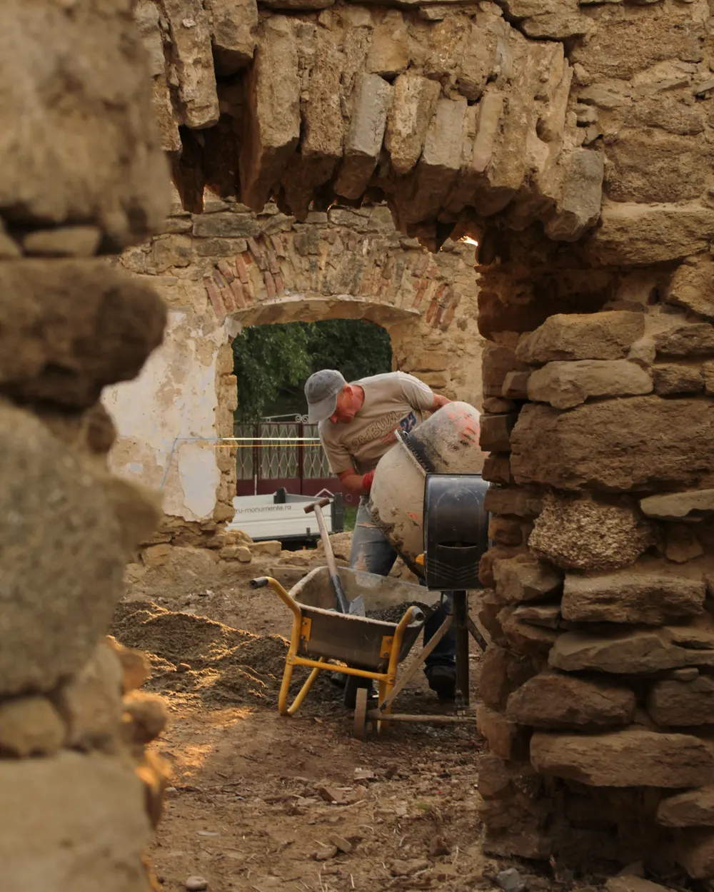 Maçon préparant du mortier à la bétonnière, vu à travers l'ouverture d'un vieux mur en pierre